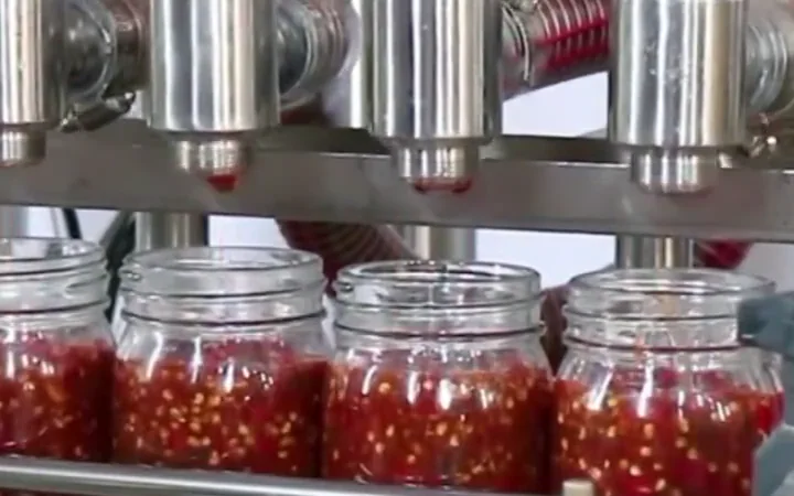 Four-head liquid filling machine filling glass jars on a production line